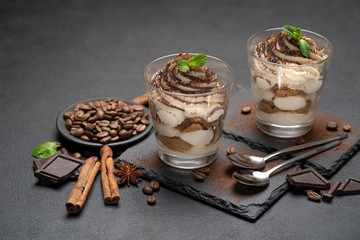 Classic tiramisu dessert in a glass on stone serving board on dark concrete background