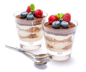 Classic tiramisu dessert with blueberries and raspberries in a glass isolated on a white background with clipping path