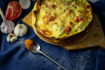delicious open French cake with chicken cauliflower onion garlic egg cream tomato pepper turmeric baked in oven on table blue cloth sieve flour