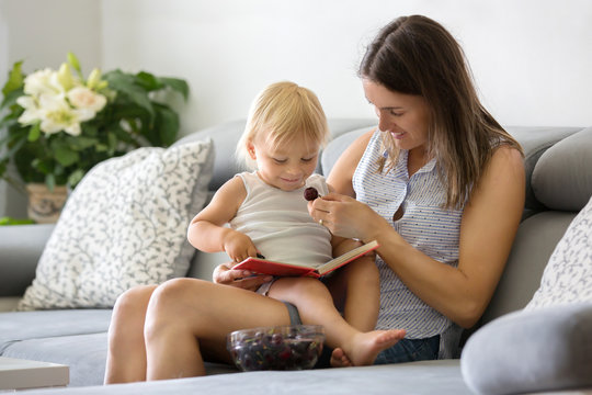 Charming mother, showing images in a book to her cute toddler baby boy at home