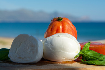 Italian mozzarella soft cheese in balls served with tomatoes and fresh basil outdoor with blue sea...