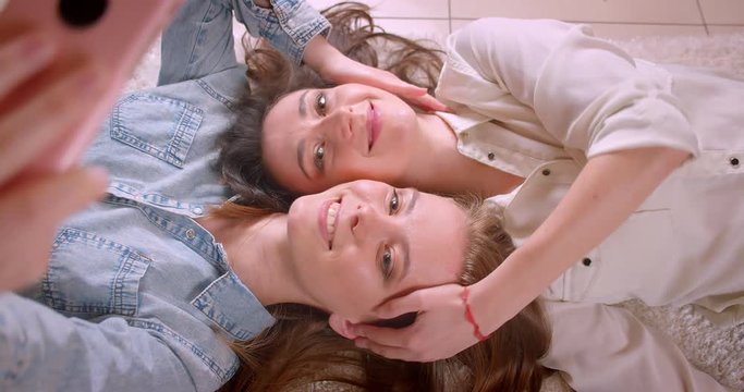 Closeup shoot of young beautiful lesbian couple taking selfies on the phone kissing happily and laying on the floor in a newly bought apartment