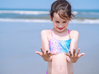 Summer beach. Little girl have a good time of resort beach. Kid playing on sandy beach. Focus on the hand . Close-up view. Summer travel and vacation concept