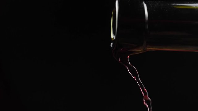 Wine. Red wine pouring from neck of bottle in wine glass over dark background. Rose wine pouring from the bottle. Slow motion