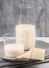 Close-up oat milk in glass bottle and glass in grey plate on grey wooden background. 