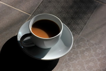 Coffee in a white glass, gray floor with morning light.