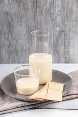 Oat milk in glass bottle and glass in grey plate on grey wooden background.
