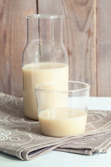 Close-up dairy free oat milk in glass bottle and glass on linen napkin on wooden background. 