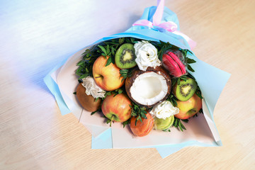 Festive packed bouquet of fruits macaroons and flowers lies on wooden table.