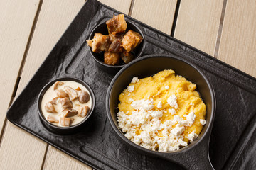 Typical Ukrainian dish polenta - Banosh with cheese and lard. Ukrainian cuisine. maize porridge with bacon, cracklings and cheese Corn porridge in plate on wooden background.