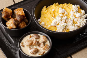 Typical Ukrainian dish polenta - Banosh with cheese and lard. Ukrainian cuisine. maize porridge with bacon, cracklings and cheese Corn porridge in plate on wooden background.