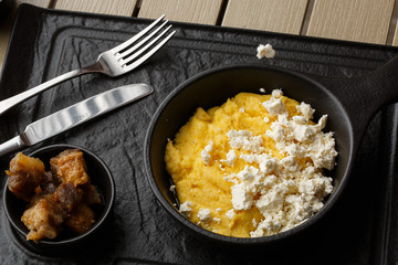 Typical Ukrainian dish polenta - Banosh with cheese and lard. Ukrainian cuisine. maize porridge with bacon, cracklings and cheese Corn porridge in plate on wooden background.