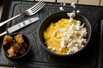 Typical Ukrainian dish polenta - Banosh with cheese and lard. Ukrainian cuisine. maize porridge with bacon, cracklings and cheese Corn porridge in plate on wooden background.