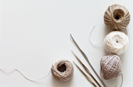 Needlework. Crochet hooks and balls of cotton yarn beige color on a white table. Тоp view, closeup, flat lay, copy space