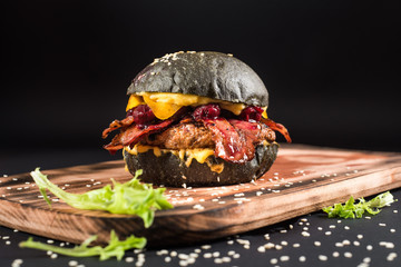 Tasty black burger with meat, bacon, cheese and cherry on the black background