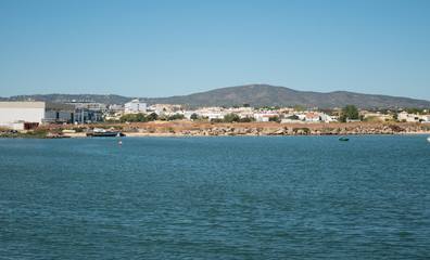 Fototapeta premium View from ocean to shore in Algarve, Portugal in summer with boat on beach, houses and hills in background.