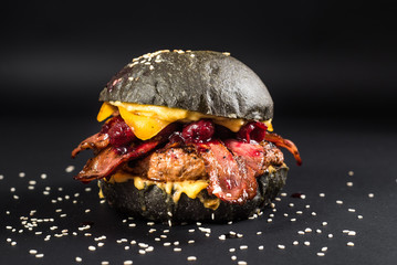 Tasty black burger with meat, bacon, cheese and cherry on the black background