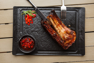 Grilled and barbecue hot pork ribs with hot chilli pepper and hot sauce on black stone background. Isolated. Dish for men. Spicy