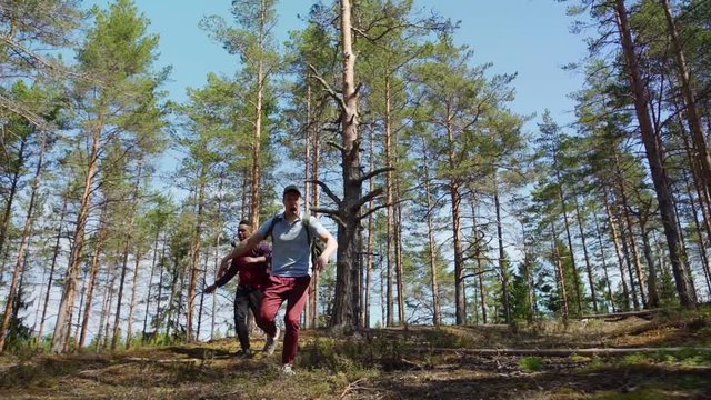 Two terribly scared young backpackers running through forest in slow motion and screaming awfully, low angle view