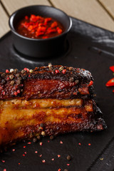 Grilled and barbecue hot pork ribs with hot chilli pepper and hot sauce on black stone background. Isolated. Dish for men. Spicy