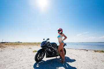 Fototapeta na wymiar Young amazing sexy woman posing near motorbike on the beach, wearing stylish crop top , shirts, have perfect fit slim tamed body and long hairs. Outdoor lifestyle portrait.