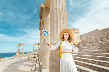 Young traveler woman with greek flag at the ancient greek ruins. Tourism in Greece concept