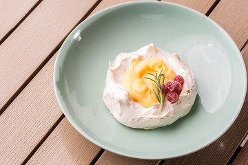 Pavlova mini cake with custard cream and fresh summer berries on green plate on wooden background. Baked meringue cake.