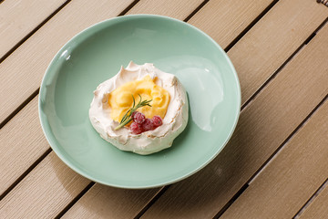 Pavlova mini cake with custard cream and fresh summer berries on green plate on wooden background. Baked meringue cake.