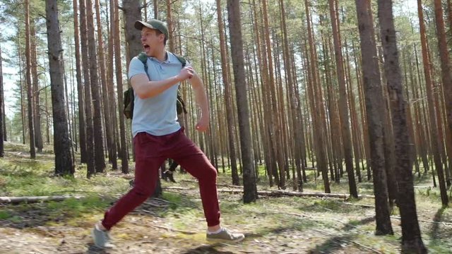 Tracking right shot of two awfully scared young men with backpacks running through forest in slow motion fleeing from danger and screaming awfully terribly