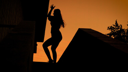 Silhouette of a beautiful young girl enjoying life dancing outdoor, fantastic summer sunset.