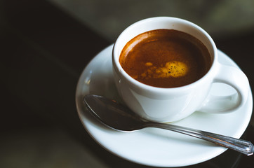 close up modern hot black coffee the espresso on dark background with coffee bubble foam pattern and texture in white cup looking and feel so delicious on glasses table in coffee shop.