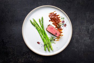 Blanched green asparagus with barbecue dry aged wagyu fillet steak and hot sauce as top view on a...