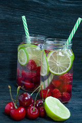 Refreshing summer drink with fruit. Drink made from cherry, raspberry, lime. Dark wooden background.