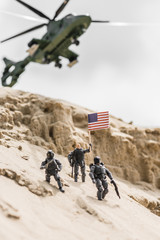 Selective focus of toy soldiers on sand hill with American flag and helicopter on background