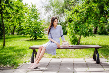 A girl of Asian appearance on a bench in a city park. Summer portrait of young Tatar on a background of green foliage
