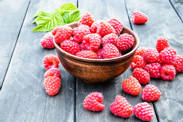Ripe red raspberries on a bowl on the background of the old dark boards. Selective focus.