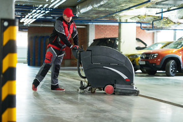 worker with machine cleaning floor in parking garage.