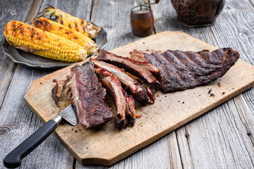 Barbecue spare ribs St Louis cut with hot rub and corn as closeup on a wooden cutting board