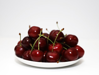 A bunch of ripe cherries with peduncles lies on a white background. Large collection of fresh red cherries. Ripe cherries background isolate
