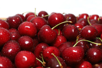 A bunch of ripe cherries with peduncles lies on a white background. Large collection of fresh red cherries. Ripe cherries background isolate