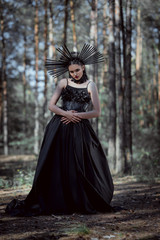 Fototapeta premium elegant woman in witch costume standing on forest background, looking at camera