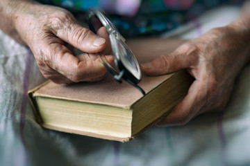 Pensioner reading a book. Hands of an elderly person close up. An elderly woman is holding a book and glasses.