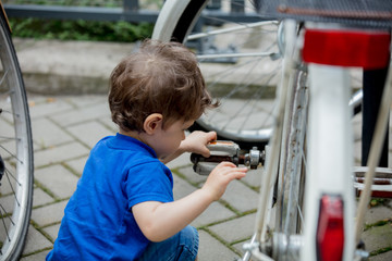 little toddler boy plays enthusiastically with big bikes on a city bike parking