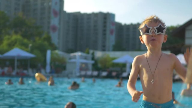Portrait of the boy in sunglasses in the form of stars dancing disco in the water park on the background of the pool with people
