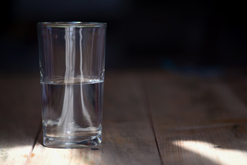 A half empty or half full glass of water on a rustic wooden table and dark background.