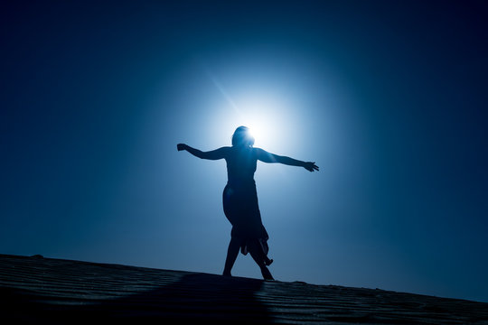 silhouette of young woman with long skirt dancing in evocative and confident way on top of desert dune at night