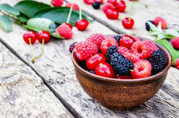 juicy fresh delicious berries raspberries, cherries, mulberries in a bowl on wooden background.