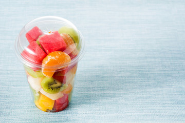 Fresh cut fruit in a plastic cup on blue background