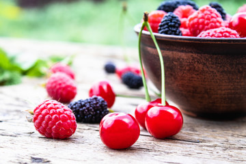 juicy fresh tasty berries raspberries, cherries, mulberries in a bowl on wooden boards on a background of green grass.