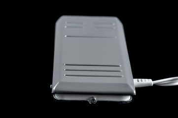 Iron gray pedal for a sewing machine with a wire on a black background, isolate